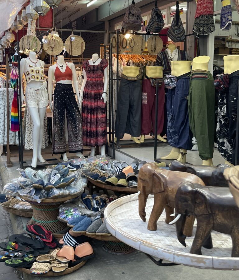 Handcrafted elephant statues with various souvenirs in the background at a Chiang Mai night market, a popular place to shop for unique Thai gifts.