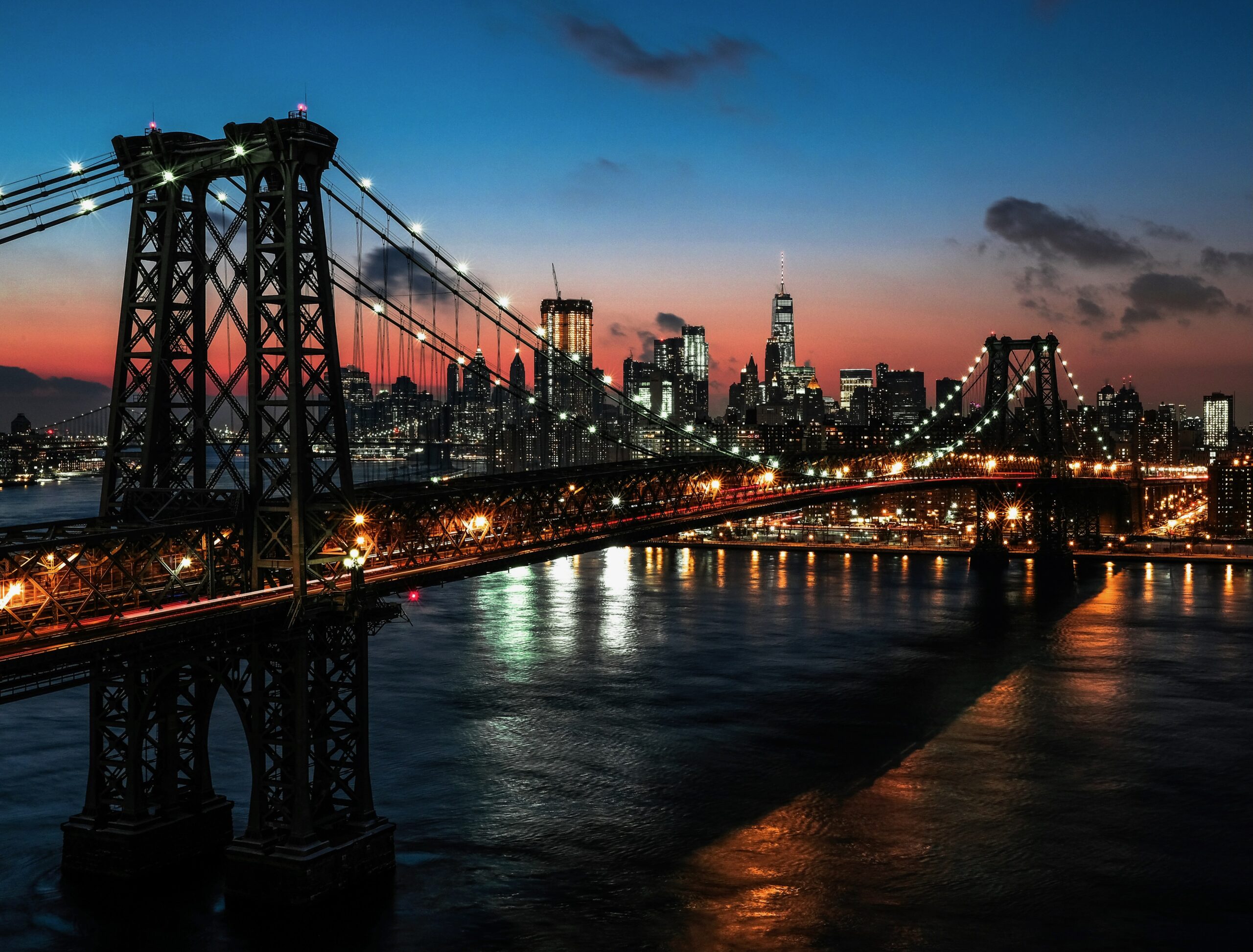Remarkable summer sunset in NYC with orange hues in the sky, featuring the Brooklyn Bridge and city skyline at dusk.