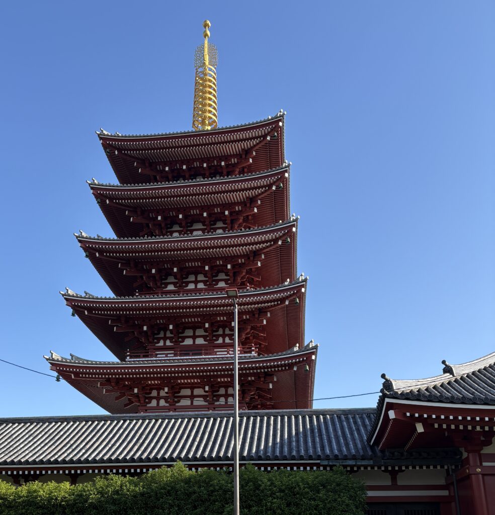 Senso-ji Temple in Tokyo standing tall under a blue sky with a traditional Japanese garden in the foreground.