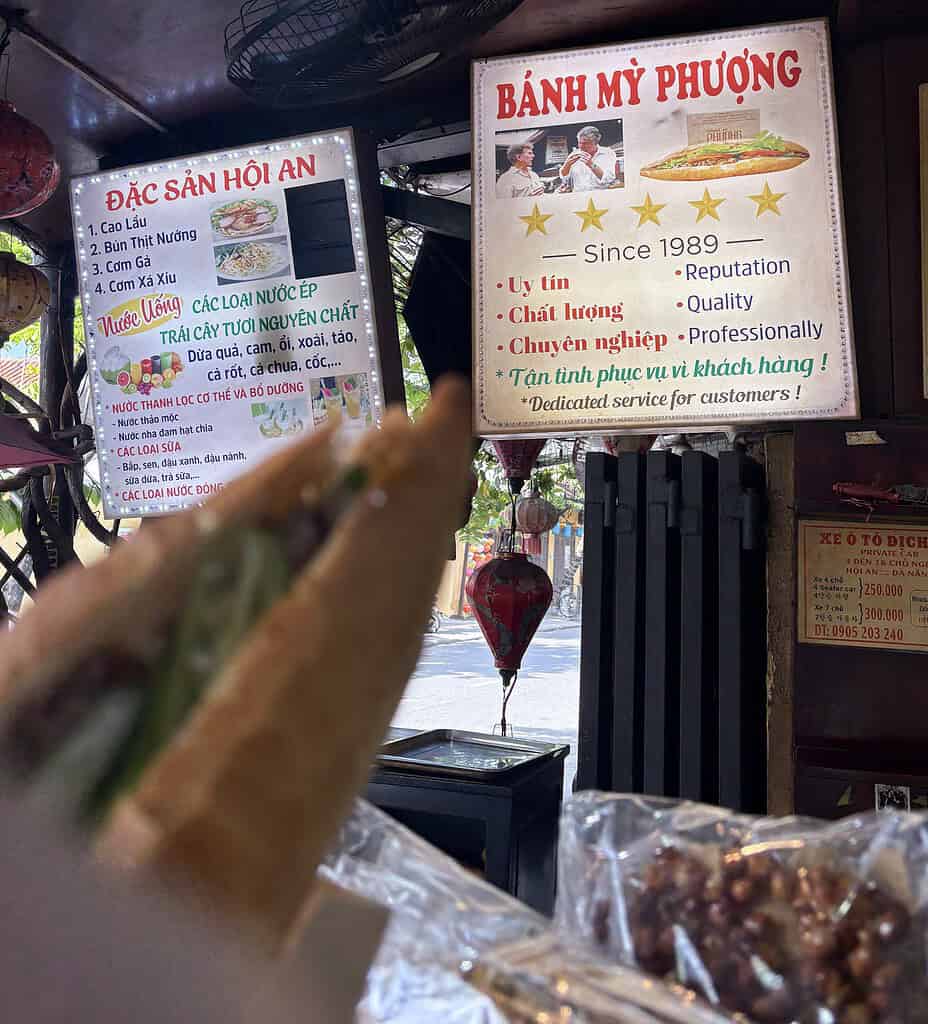 A banh mi sandwich held in front of the Anthony Bourdain poster at Banh Mi Phuong in Hoi An.
