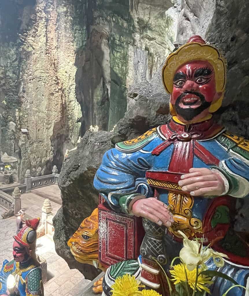 Brightly painted red, blue, and yellow statues inside a cave at the Marble Mountains in Da Nang, featuring non-Buddha figures with intricate detailing.