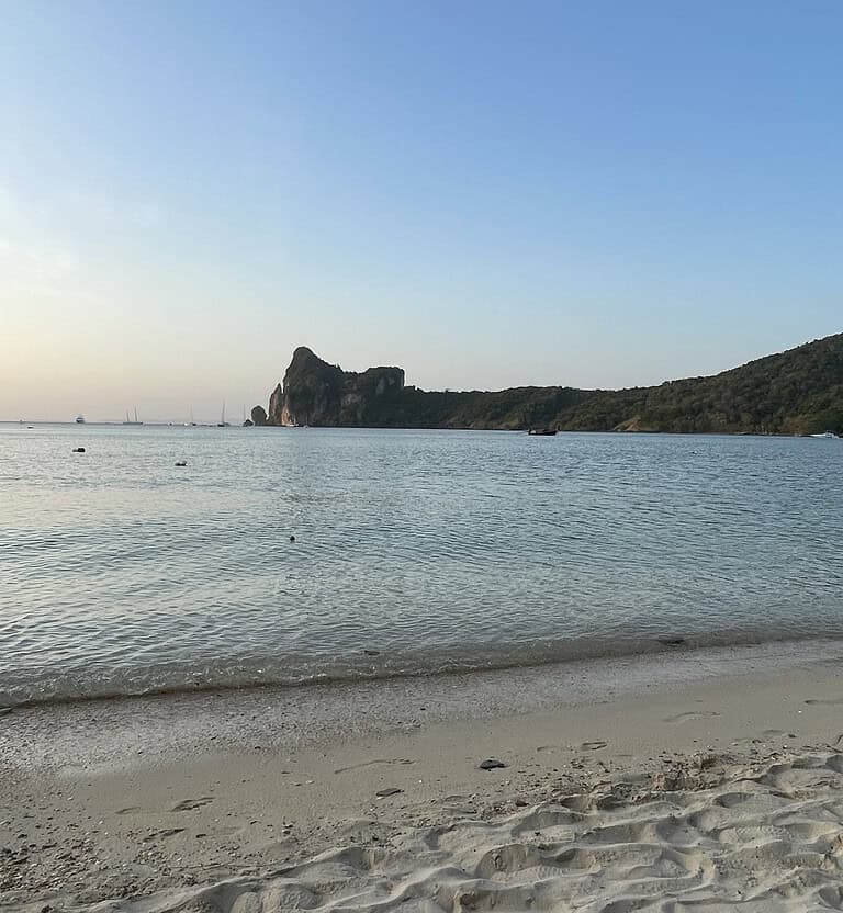 Peaceful evening view of Loh Dalum Bay with calm waters and limestone cliffs in the distance on Phi Phi Island.