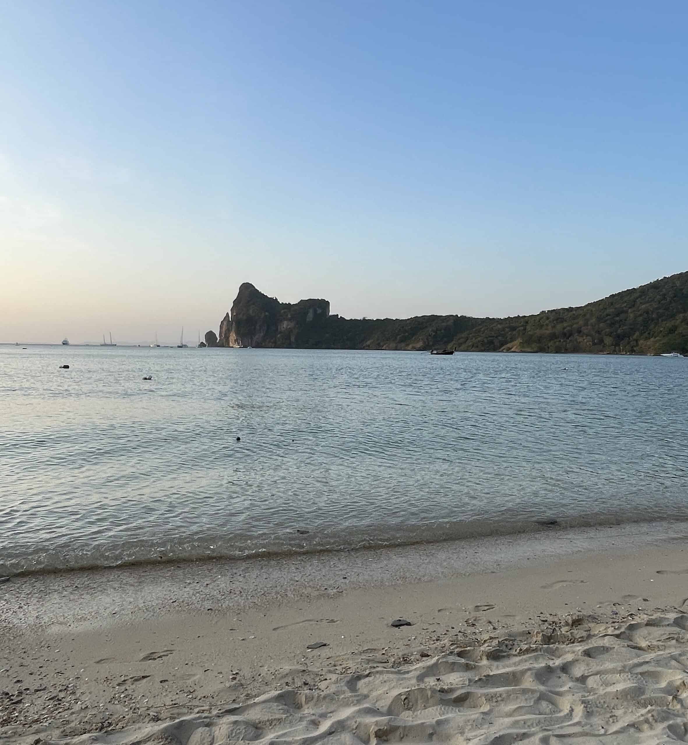 Peaceful evening view of Loh Dalum Bay with calm waters and limestone cliffs in the distance on Phi Phi Island.