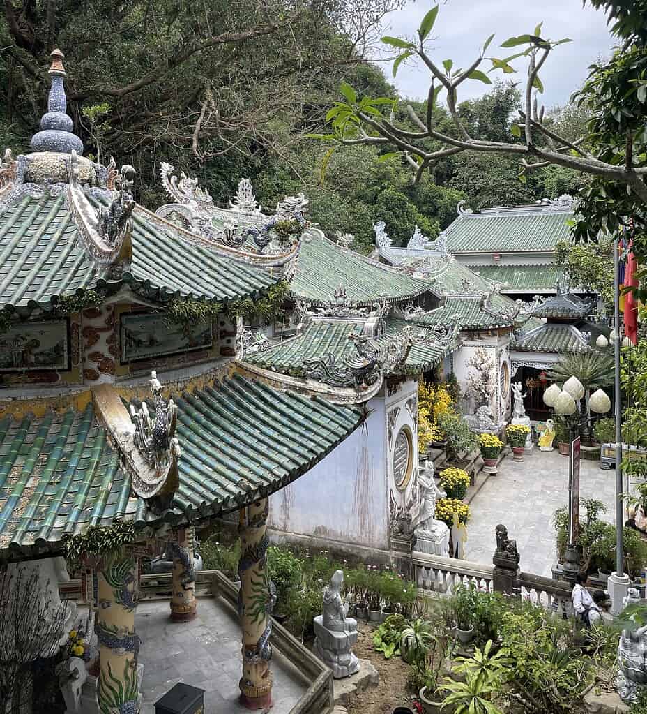 Multiple pagodas with unique rooftop architecture surrounded by Buddha statues and lush plants at the Marble Mountains in Da Nang, Vietnam.