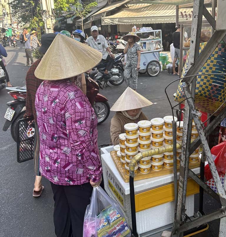 Two women wearing traditional Vietnamese conical hats shopping at a busy street market in Saigon, Vietnam