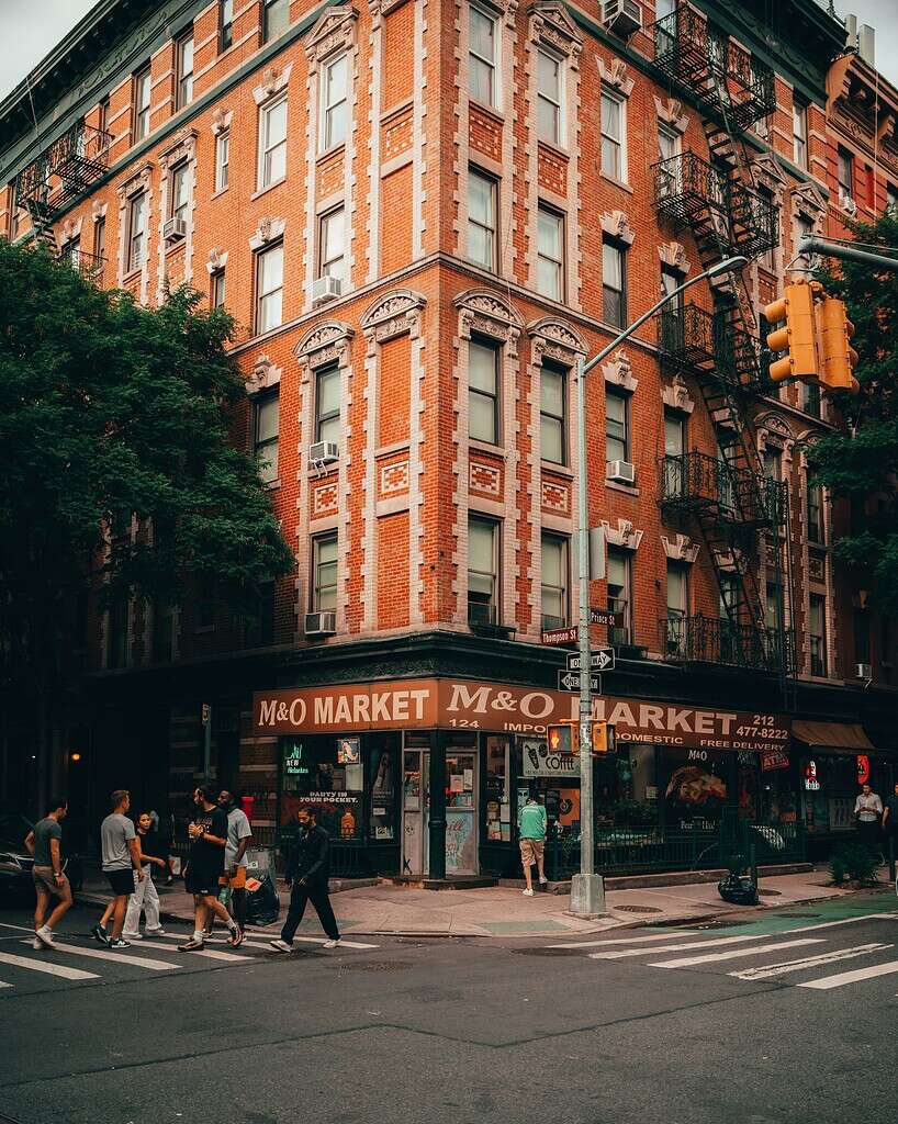 Locals and tourists walking in NYC with a corner store in the background
