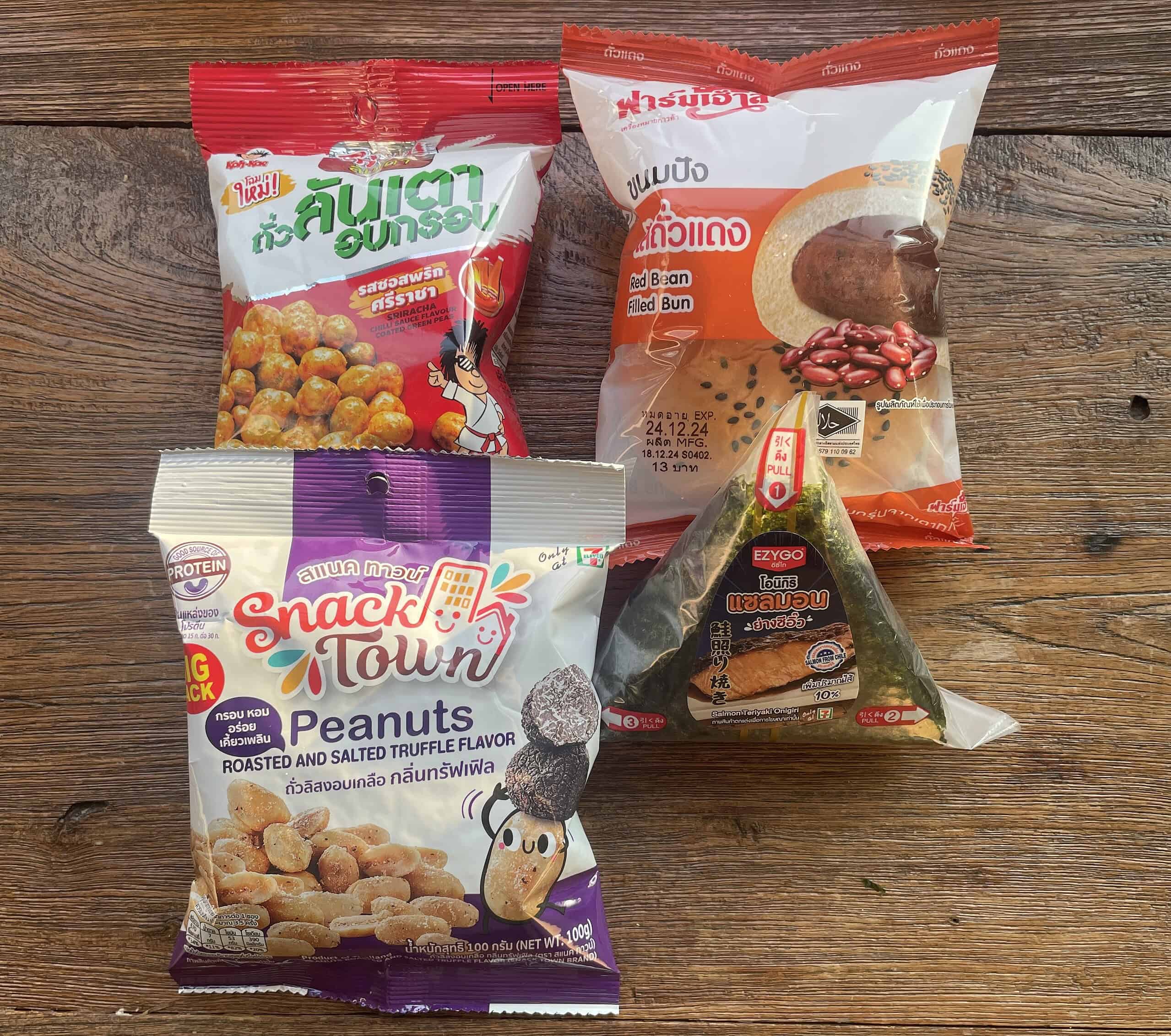 Assorted Thailand 7-Eleven snacks including truffle-flavored peanuts, red bean bun, coconut nut crackers, and an Onigiri roll
