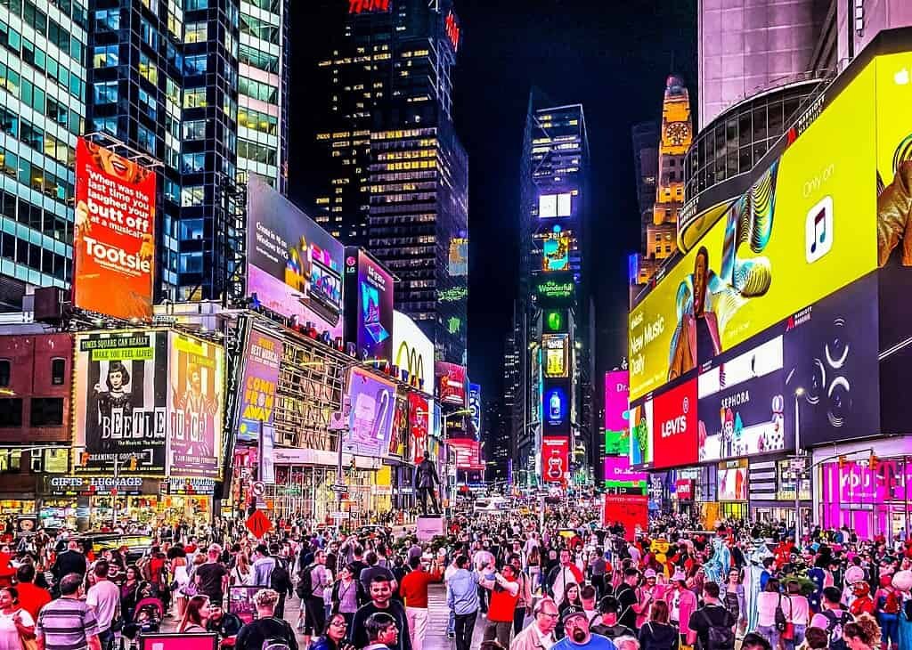 Crowds of people in Times Square at night with bright advertising billboards all around