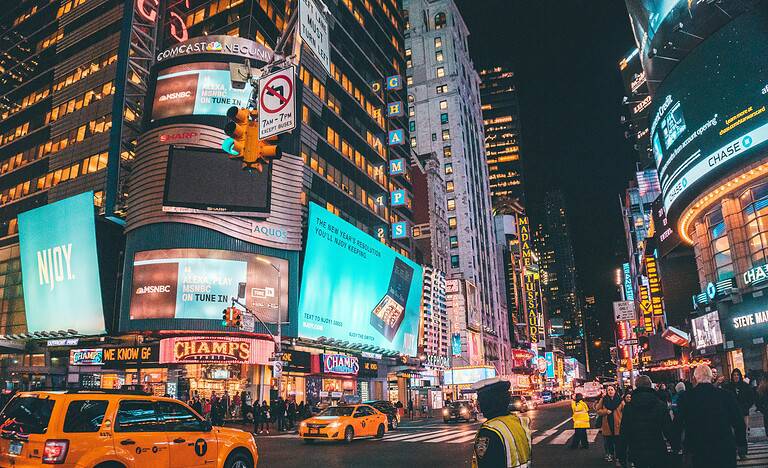 Times Square in NYC with yellow cabs, tourists walking, and locals on a busy street