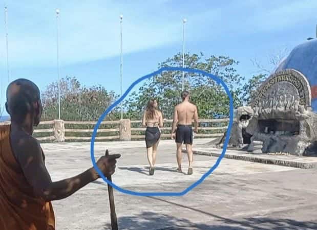 Tourists wearing a bikini and no shirt while walking through a Buddhist temple in Thailand, showing inappropriate clothing in a sacred space