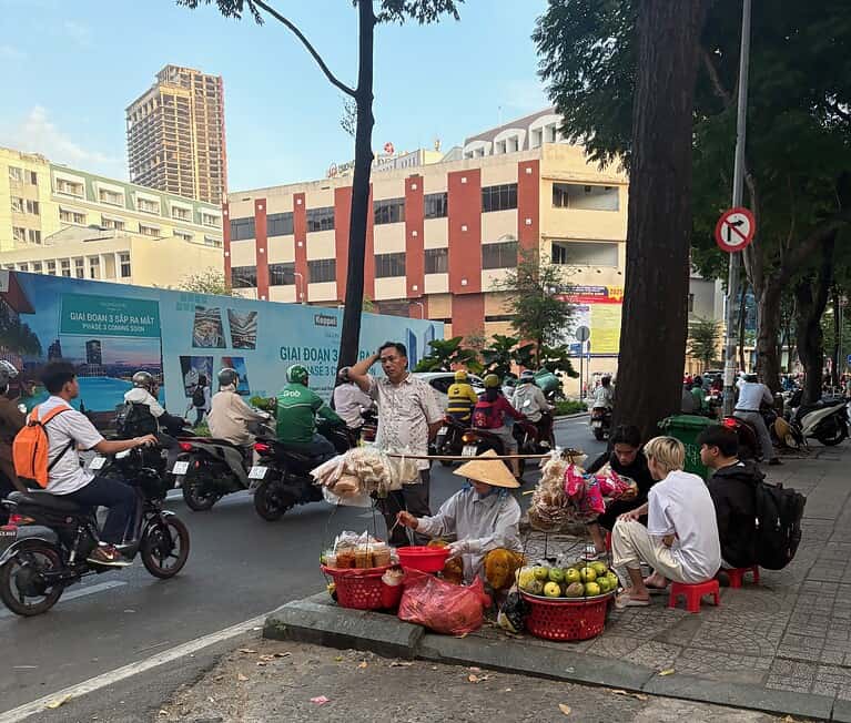 A woman street vendor in Saigon selling on the sidewalk with scooters and customers passing by in the background