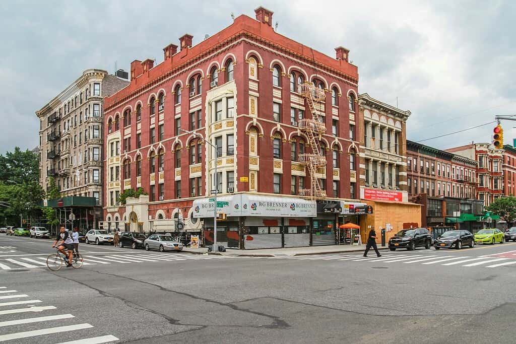 Four-way street intersection in Harlem with brownstone buildings on a sunny summer day
