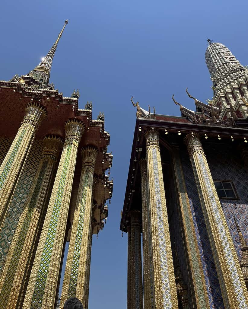 Two ornate temples at the Grand Palace in Bangkok, Thailand, under clear blue skies