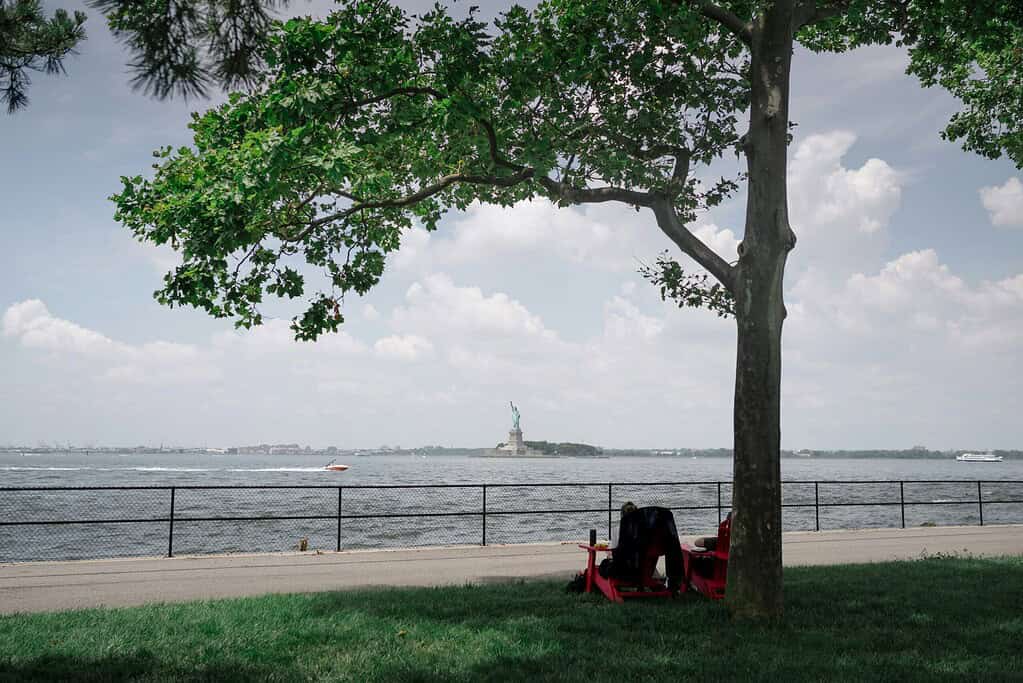 Scenic view from Governors Island, NYC, facing the Statue of Liberty across New York Harbor under a clear blue sky.