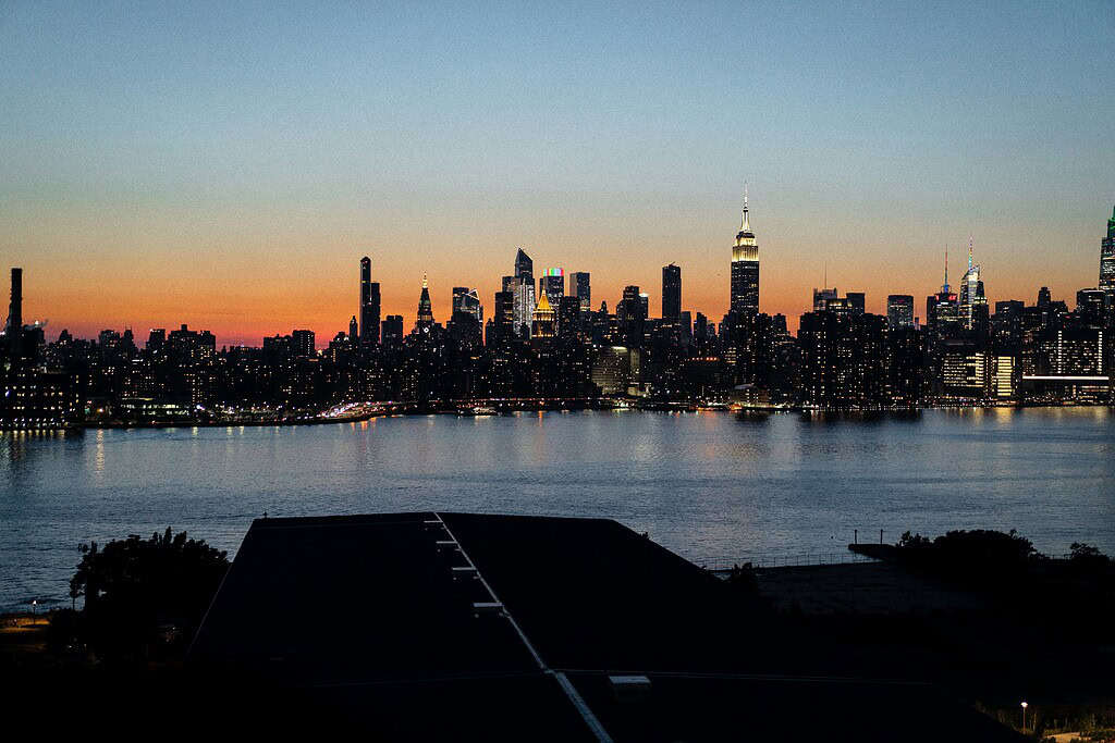 Golden hour sunset over the classic New York City skyline, with iconic skyscrapers glowing in warm light under a soft orange sky.