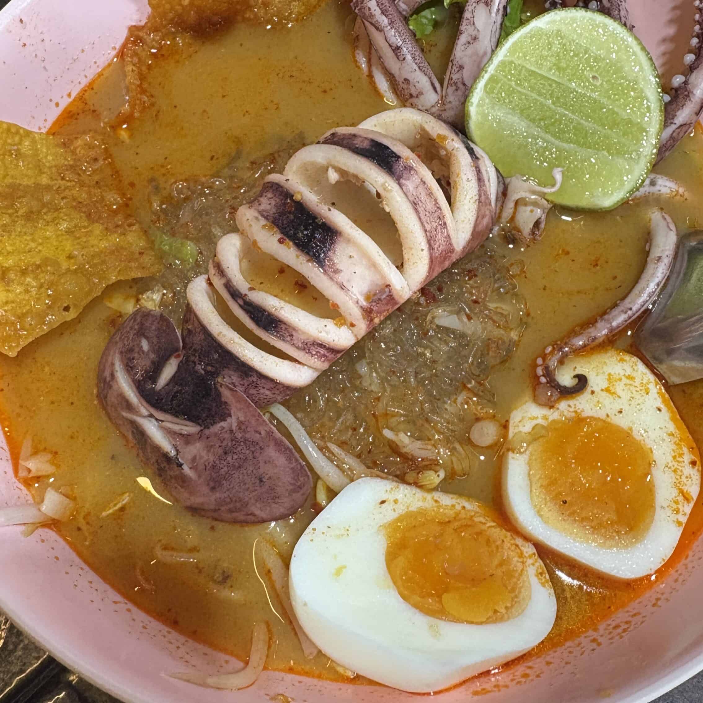 Close-up of Thai Tom Yum soup with whole prawns, lime, and crispy wonton in a white bowl, Thailand
