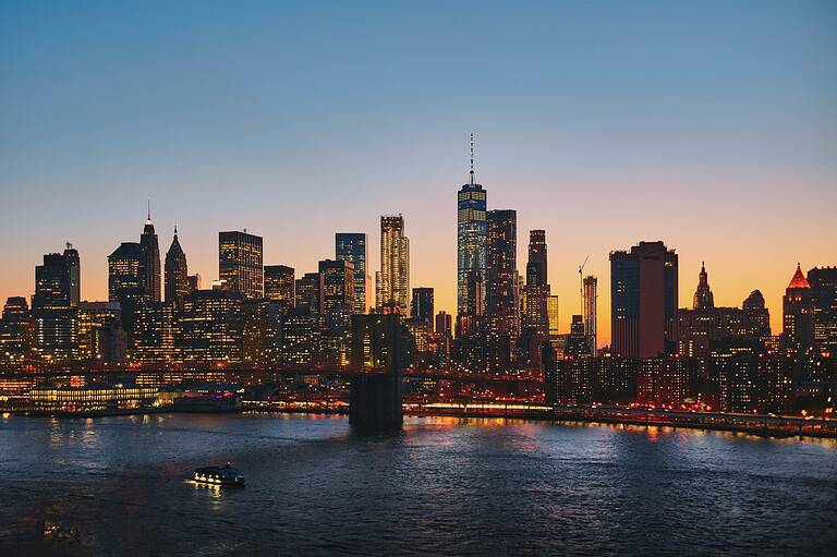 NYC skyline at sunset with the Brooklyn Bridge and One World Trade Center lit up over the East River