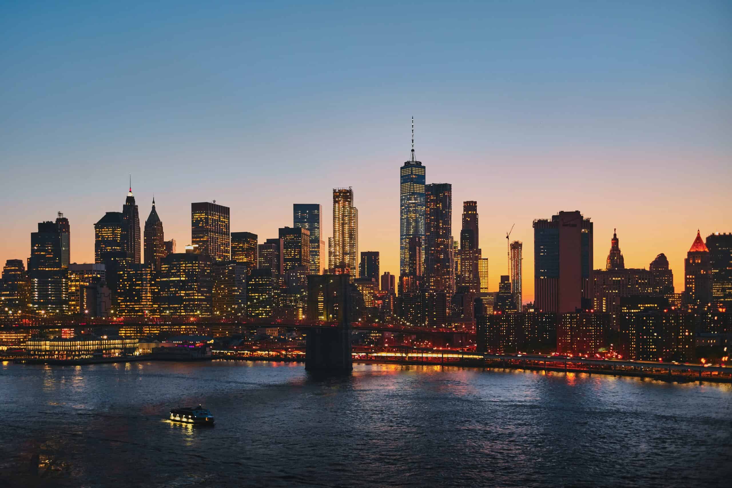 NYC skyline at sunset with the Brooklyn Bridge and One World Trade Center lit up over the East River