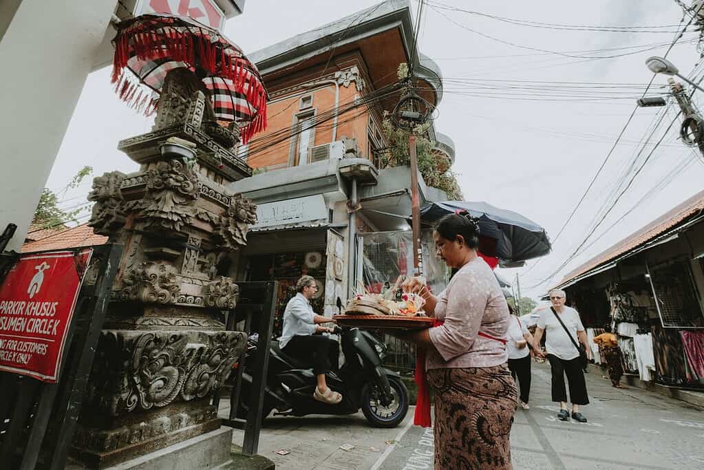 a woman handing out an offering to a small temple on the street in Bali